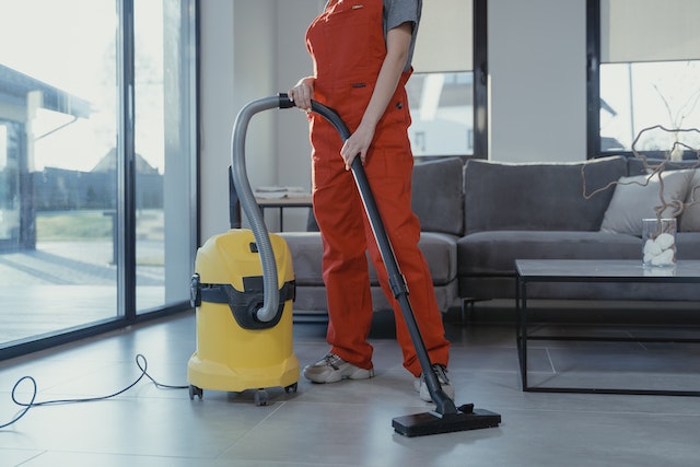 A person wearing orange coveralls vacuuming the living room floor.